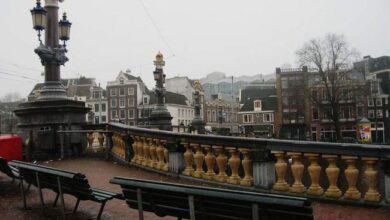 Sztucznie rysowany most w Amsterdamie z widokiem na zabytkowe budynki i ulicę w deszczową pogodę, idealne na architektoniczne inspiracje i odzwierciedlenie stylu europejskiego miasta.