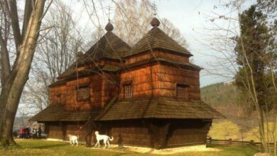 Tradycyjny drewniany kościół w otoczeniu natury, z charakterystyczną architekturą sakralną i malowniczym otoczeniem, idealny na wycieczki i poznanie historycznego dziedzictwa.