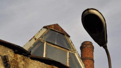 Burzowa rura na dachu z widokiem na stary komin przemysłowy, zdjęcie architektury i przemysłowej konstrukcji, z pochmurnym niebem w tle, idealne do projektu modernizacji obiektów przemysłowych.