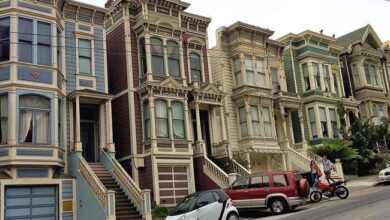 Unikalne, kolorowe kamienice na stromej ulicy w San Francisco, wpisujące się w architekturę victorian i bay window, z samochodami na ulicy, idealne do artykułów o nieruchomościach i architekturze.