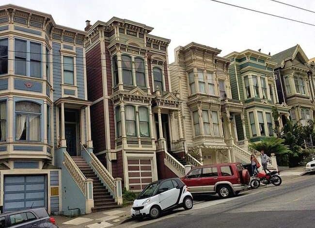 Unikalne, kolorowe kamienice na stromej ulicy w San Francisco, wpisujące się w architekturę victorian i bay window, z samochodami na ulicy, idealne do artykułów o nieruchomościach i architekturze.