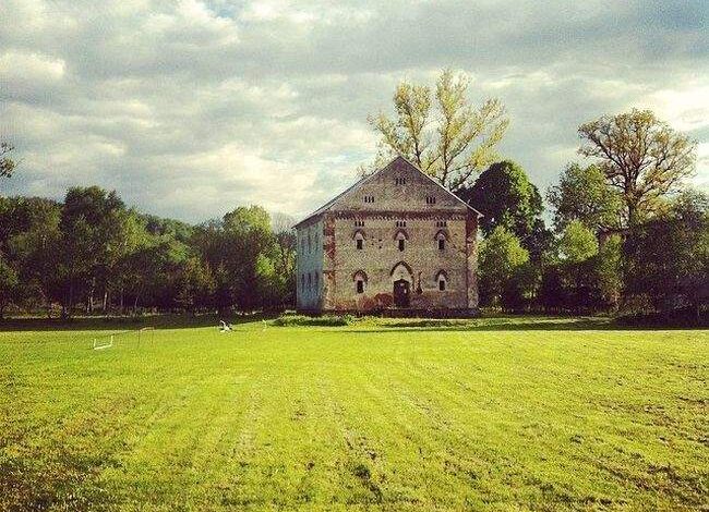 Stara ceglana budowla na zielonym polu, otoczone drzewa, krajobraz wiejski, zabytkowa architektura, idealne miejsce na relaks na łonie natury.