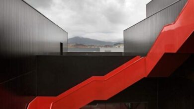 Czarne i czerwone schody na tle nowoczesnej architektury z widokiem na góry i port, idealne do opisu kreatywnych przestrzeni i designu na stronie PaniDyrektor.pl.