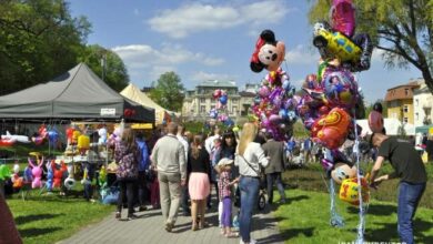 Kolorowy festyn na świeżym powietrzu z balonami, atrakcjami i tłumem odwiedzających, idealne wydarzenie rodzinne i integracyjne w parku.