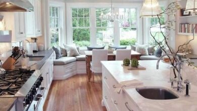 Nowoczesna, jasna kuchnia z dużymi oknami, eleganckimi szafkami i wyspą z blatem marmurowym, idealne miejsce do gotowania i rodzinnych spotkań, przytulne i funkcjonalne wnętrze.