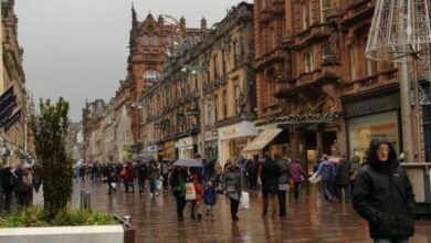 Londyńska ulica w deszczowy dzień z tłumem przechodniów, stare kamienice i miejskie dekoracje, atmosfera miejskiej burzy, mokre chodniki, popularny klimat miasta, świąteczne ozdoby na ulicach, dynamiczny krajobraz urbanistyczny, stylowa architektura.