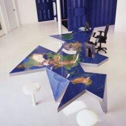 Zdjęcie nowoczesnego biura z unikalnym stołem w kształcie mapy świata, biurkami i wygodnymi krzesłami, idealne do pracy i nauki międzynarodowej, kreatywne rozwiązania aranżacji przestrzeni biurowej.