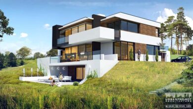 Nowoczesny dom jednorodzinny z dużymi oknami i tarasem na zielonym wzgórzu, otoczony naturą, idealny do życia w zgodzie z przyrodą.