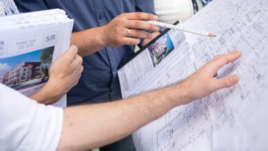 Prezes i architekt omawiający projekty architektoniczne na placu budowy, pojawia się dokumentacja budowlana, plany mieszkań i wizualizacje. Współpraca architektoniczna i nadzór inwestycyjny.