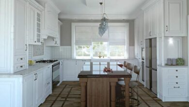 Wyspa kuchenna z blatem z kamienia, eleganckie białe szafki kuchenne w stylu klasycznym, duże okno zapewniające naturalne oświetlenie, wnętrze nowoczesnej kuchni w stylu skandynawskim.